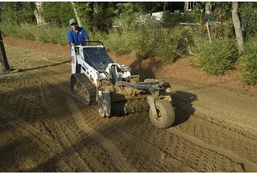 Hydraulic soil conditioner on a skid steer loosening subsoil before lawn seeding